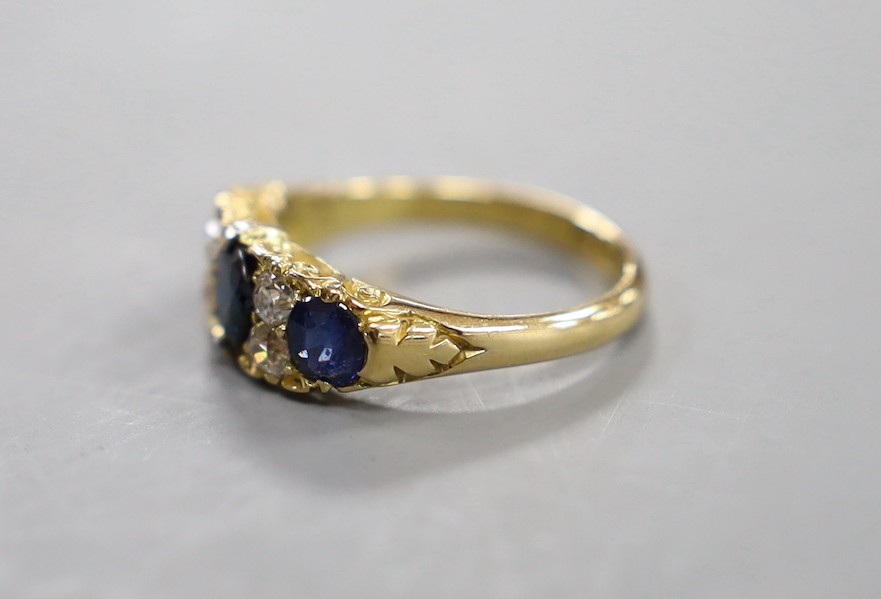 A late Victorian 18ct gold, three stone sapphire, and four stone diamond set half hoop ring, with carved setting, size O, gross weight 4.3 grams.